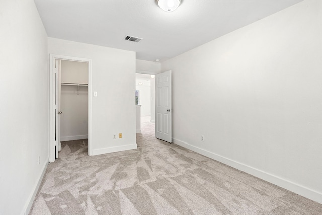 unfurnished bedroom with baseboards, visible vents, light colored carpet, a walk in closet, and a closet