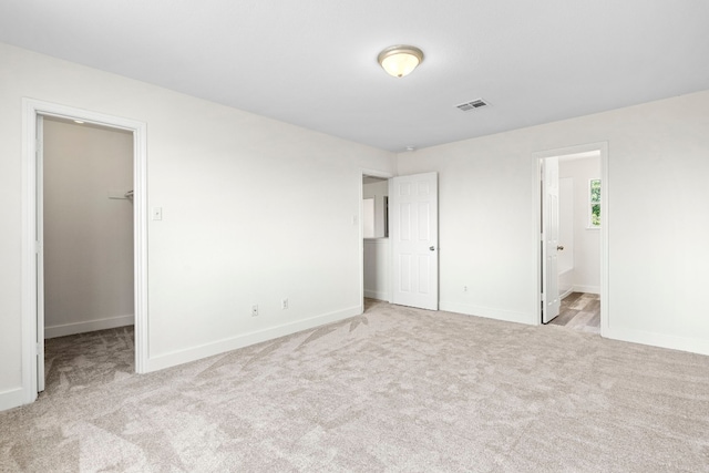 unfurnished bedroom with a spacious closet, carpet flooring, visible vents, and baseboards