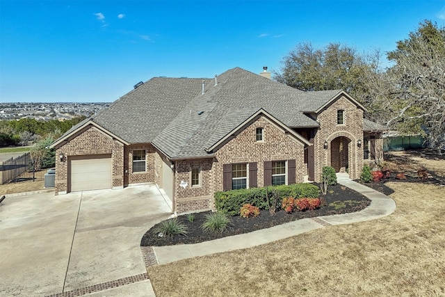 french country inspired facade with a garage, brick siding, fence, driveway, and roof with shingles