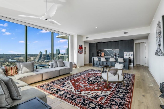 living room featuring a city view, a ceiling fan, visible vents, expansive windows, and light wood finished floors