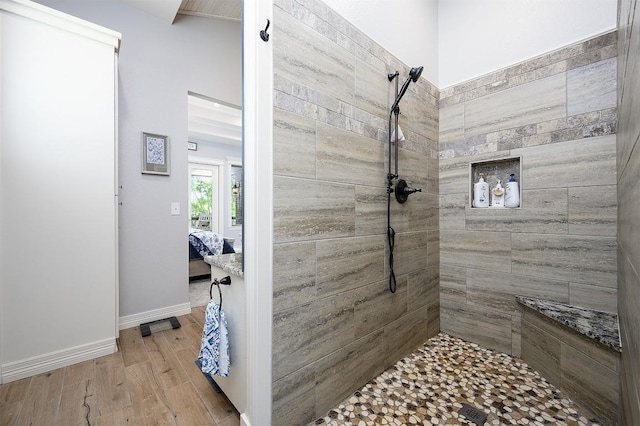 bathroom featuring baseboards, wood finished floors, a tile shower, and connected bathroom