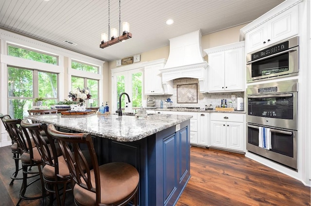 kitchen with tasteful backsplash, custom exhaust hood, stainless steel appliances, white cabinetry, and a sink