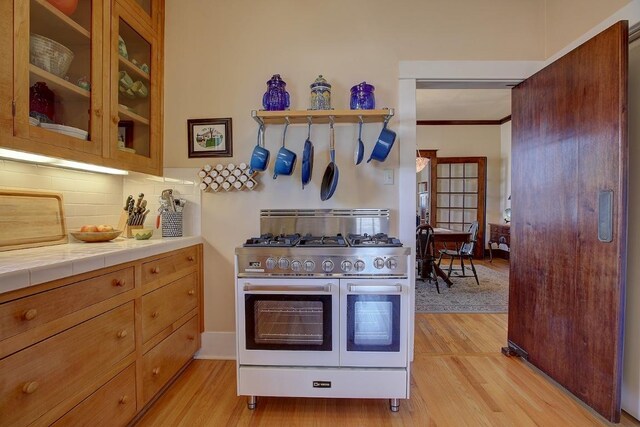 kitchen with range with two ovens, light wood-type flooring, glass insert cabinets, and tasteful backsplash