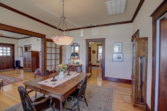 dining room with ornamental molding, light wood-style flooring, visible vents, and baseboards