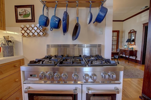 room details featuring decorative backsplash, range with two ovens, stainless steel countertops, wood finished floors, and crown molding