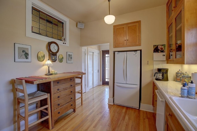 kitchen with light countertops, light wood-style flooring, decorative backsplash, glass insert cabinets, and white appliances