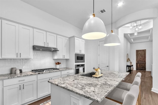 kitchen with under cabinet range hood, stainless steel appliances, white cabinetry, visible vents, and dark wood-style floors