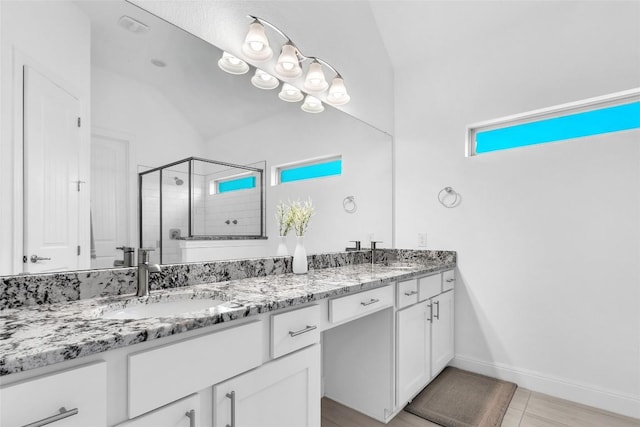 full bathroom with double vanity, a shower stall, baseboards, and a sink