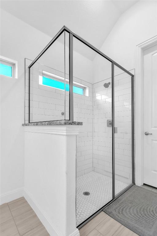 full bathroom with lofted ceiling, a shower stall, and baseboards