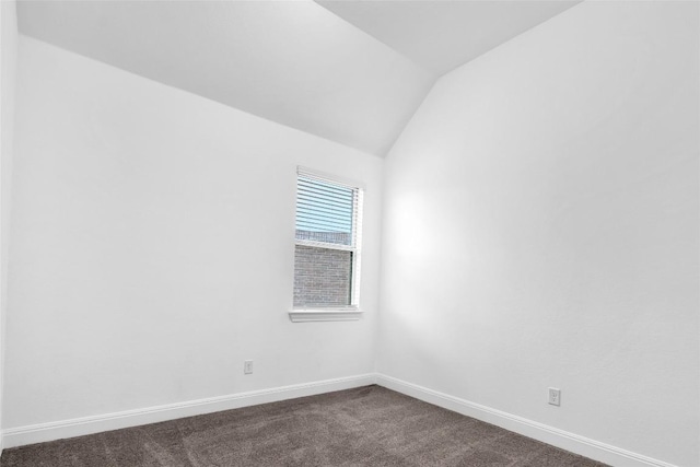 unfurnished room featuring vaulted ceiling, dark carpet, and baseboards