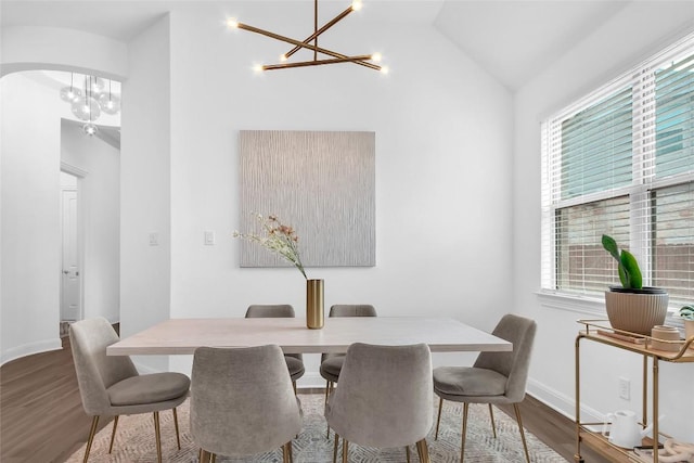 dining area featuring a chandelier, arched walkways, wood finished floors, baseboards, and vaulted ceiling