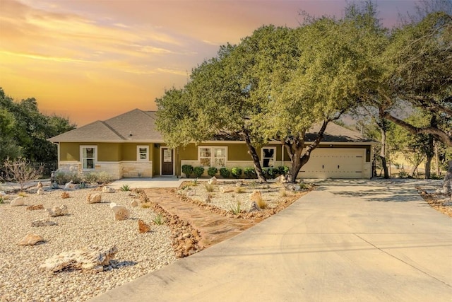 ranch-style home featuring stone siding, stucco siding, concrete driveway, and a garage