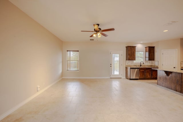 unfurnished living room with baseboards, a ceiling fan, and a sink