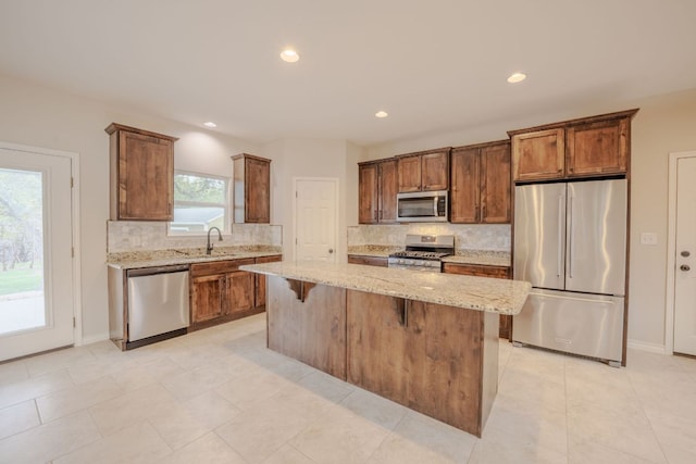 kitchen featuring a kitchen island, light stone countertops, decorative backsplash, stainless steel appliances, and a sink