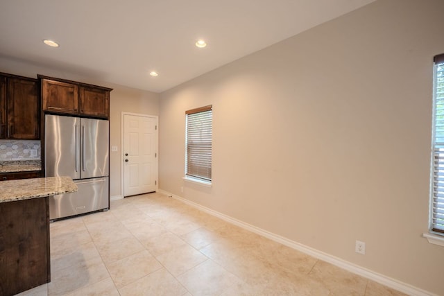 kitchen with backsplash, freestanding refrigerator, baseboards, dark brown cabinets, and light stone countertops