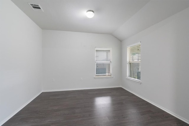 spare room with dark wood-type flooring, visible vents, vaulted ceiling, and baseboards