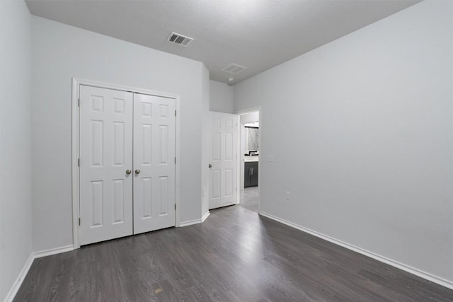 unfurnished bedroom with baseboards, visible vents, dark wood finished floors, and a closet