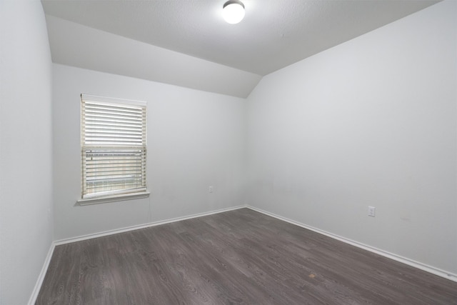 empty room featuring dark wood-style flooring, vaulted ceiling, and baseboards