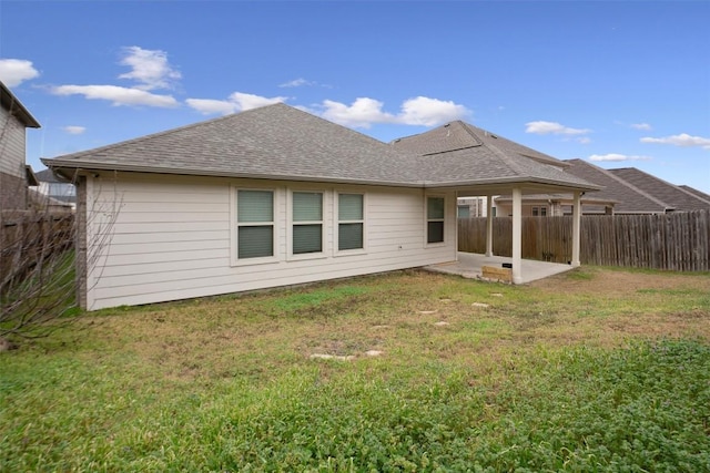 rear view of property with a patio area, roof with shingles, fence, and a yard