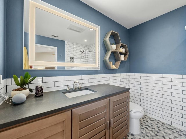 bathroom featuring toilet, visible vents, tile walls, and vanity