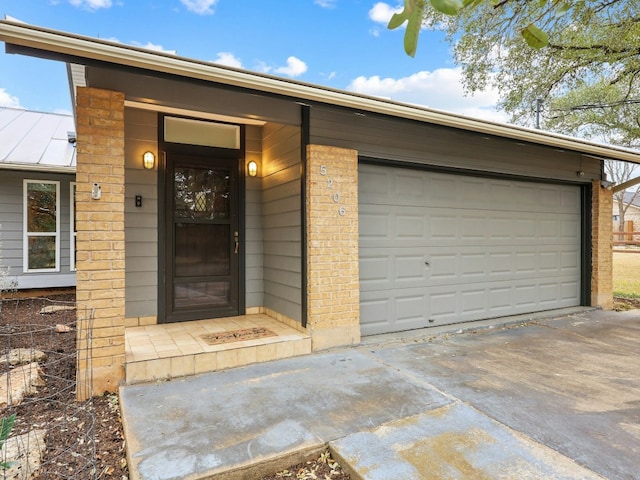 entrance to property featuring driveway, brick siding, and an attached garage