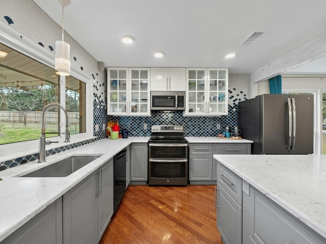 kitchen with gray cabinetry, a sink, visible vents, appliances with stainless steel finishes, and backsplash