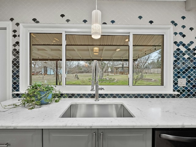 kitchen featuring a wealth of natural light, light stone counters, a sink, gray cabinetry, and stainless steel dishwasher