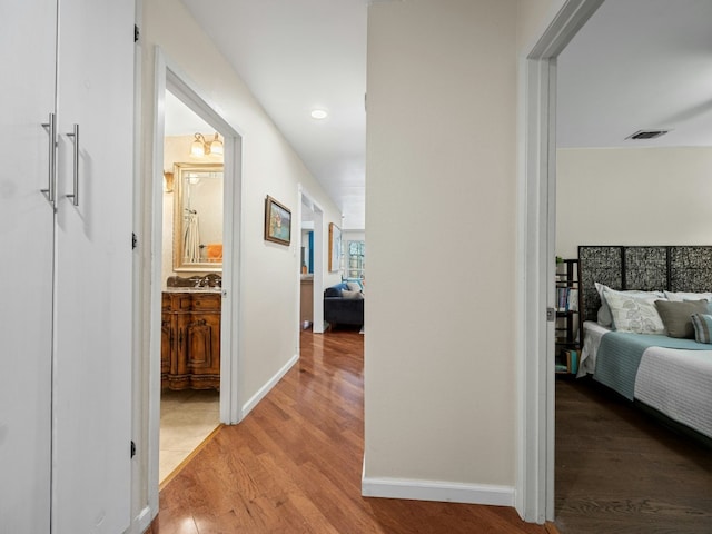 hall featuring wood finished floors, visible vents, and baseboards