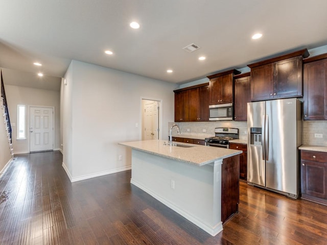 kitchen featuring dark wood-style floors, stainless steel appliances, visible vents, a sink, and an island with sink