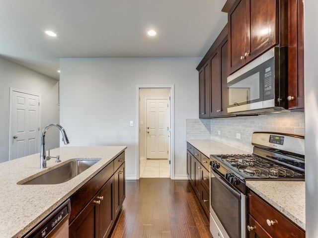 kitchen featuring light stone counters, backsplash, appliances with stainless steel finishes, dark brown cabinetry, and a sink