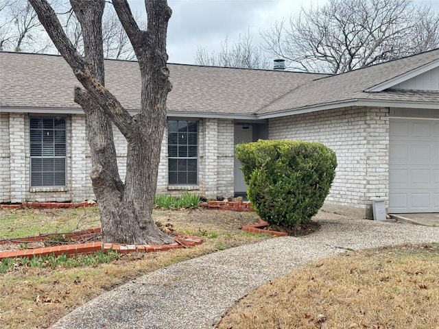 view of exterior entry with an attached garage, brick siding, and roof with shingles