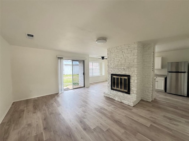 unfurnished living room featuring visible vents, baseboards, ceiling fan, wood finished floors, and a brick fireplace