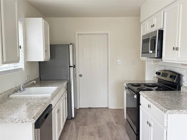 kitchen with stainless steel appliances, a sink, white cabinetry, light wood-style floors, and light countertops