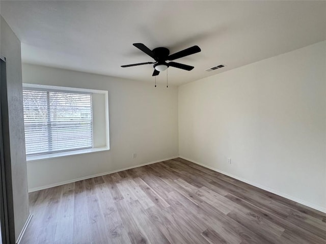 empty room featuring ceiling fan, wood finished floors, visible vents, and baseboards