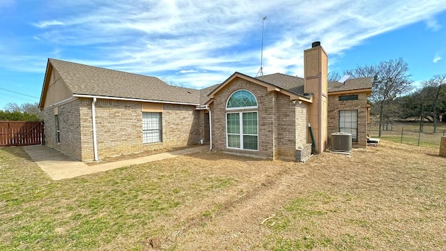 back of house with central AC, brick siding, fence, a yard, and a chimney