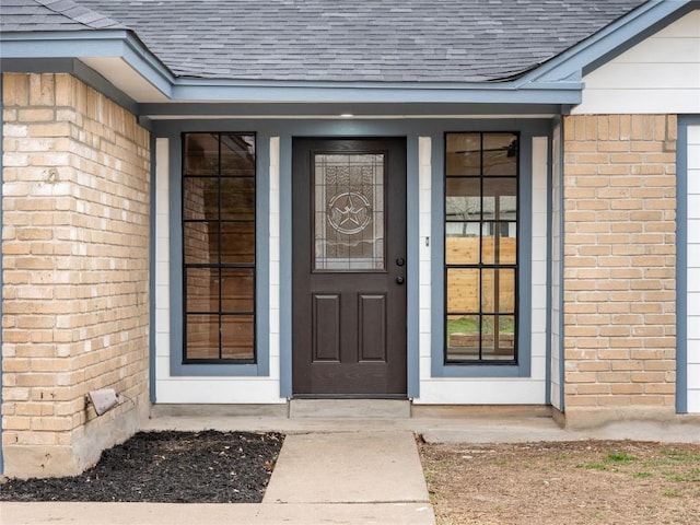 doorway to property featuring brick siding and roof with shingles