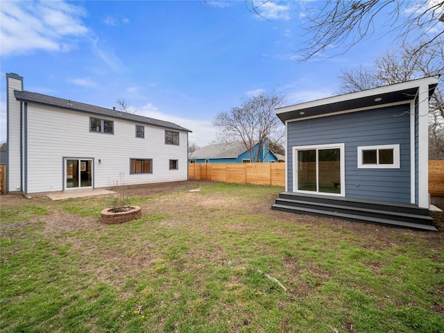 rear view of property featuring a yard, a chimney, fence, and a fire pit