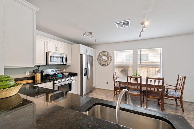 kitchen with appliances with stainless steel finishes, dark stone countertops, light wood-style floors, white cabinetry, and a sink