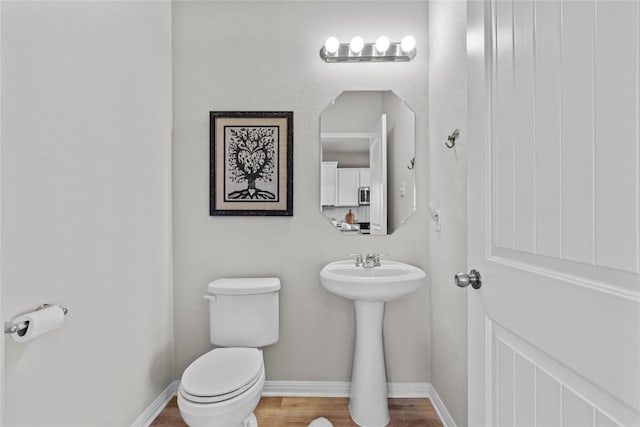 half bathroom featuring wood finished floors, toilet, and baseboards