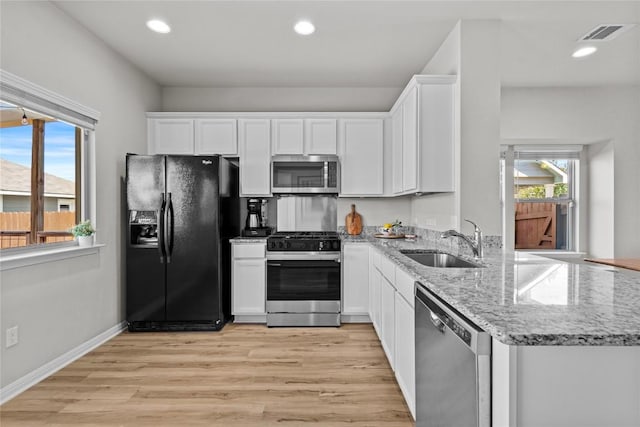 kitchen with stainless steel appliances, light wood-style flooring, white cabinetry, a sink, and light stone countertops