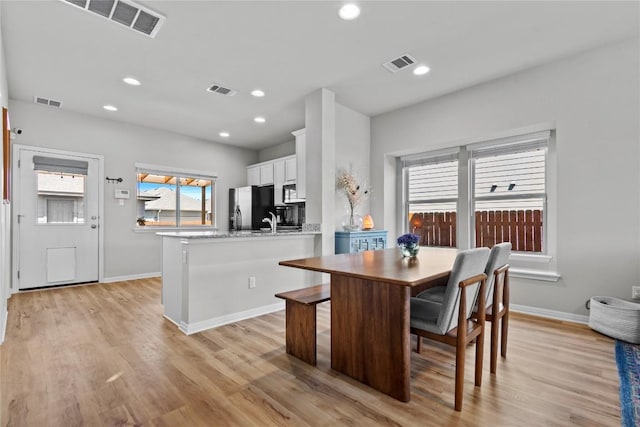 kitchen with visible vents, light wood-style flooring, white cabinets, a peninsula, and black fridge