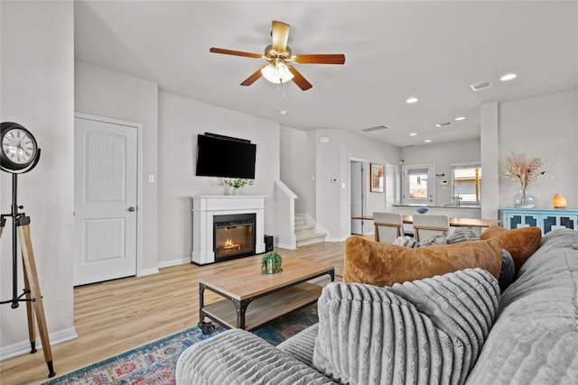 living area with light wood-style floors, a glass covered fireplace, visible vents, and recessed lighting