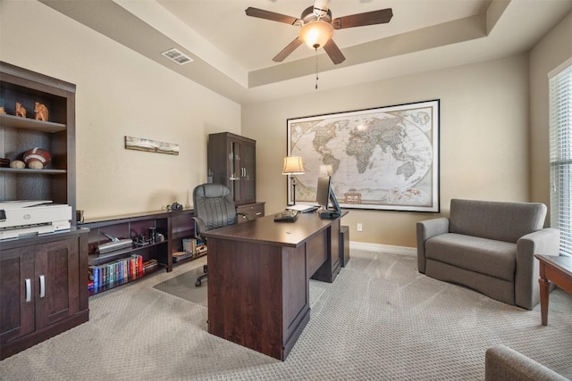 home office with light carpet, baseboards, visible vents, a raised ceiling, and a ceiling fan