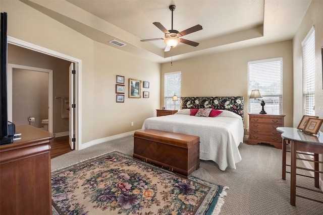 carpeted bedroom featuring ceiling fan, a tray ceiling, visible vents, and baseboards