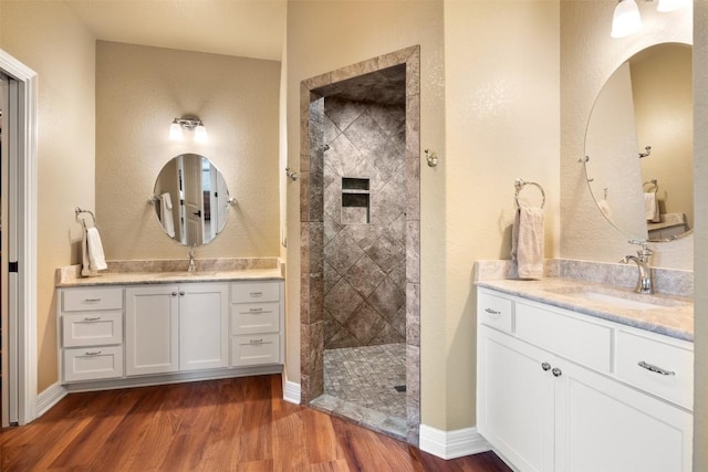 full bathroom with two vanities, a walk in shower, a sink, and wood finished floors