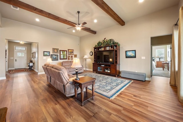 living area with beamed ceiling, wood finished floors, visible vents, and baseboards