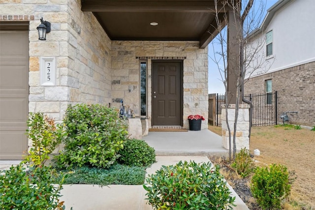 doorway to property with stone siding, an attached garage, and fence