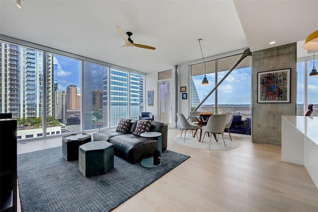 living area featuring a wall of windows, a view of city, ceiling fan, and wood finished floors