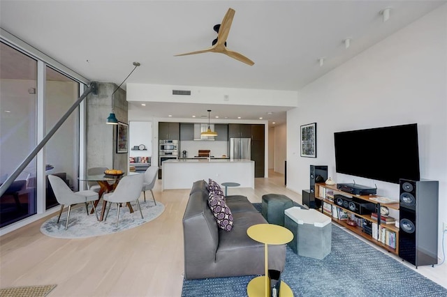 living area featuring a wall of windows, light wood-type flooring, visible vents, and a ceiling fan