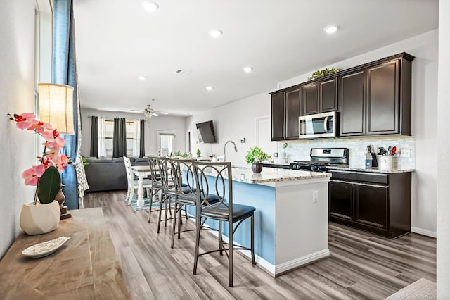 kitchen with a breakfast bar area, tasteful backsplash, appliances with stainless steel finishes, open floor plan, and a kitchen island with sink